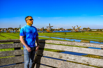 Side profile of a traveler wearing sunglasses and blue shirt admiring the Dutch countryside landscape.