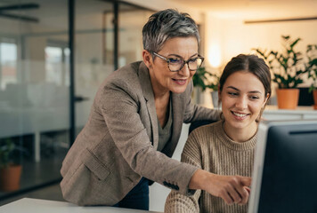 Two colleagues work together at a computer in a bright modern office space