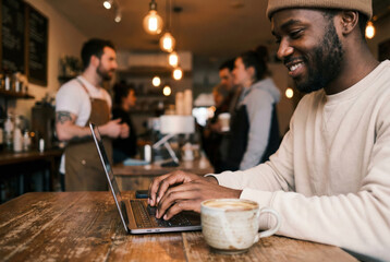 Man works on laptop in a busy cafe while sipping coffee with a smile
