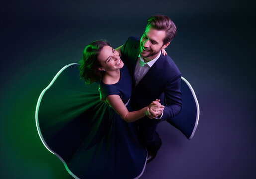 Happy elegant couple dancing and spinning in formal wear, joyful romantic celebration under dramatic green purple neon studio lighting, high angle view