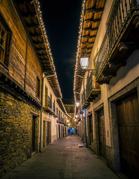 calle estrecha de un casco antiguo, iluminada con luces navide&ntilde;as c&aacute;lidas que bordean los tejados y balcones de edificios de piedra y madera, creando un ambiente festivo y acogedor durante la noche.