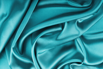 Fototapeta premium Crumpled, wrinkled turquoise colored glossy silk satin with wave drapery.. Shiny smooth fabric with soft folds, cloth texture . Elegant rich background, wallpaper, backdrop. Flat lay, top view