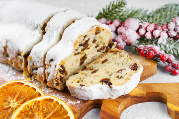 Traditional Christmas stollen, sweet fruit loaf sliced on wooden board, dusted with powdered sugar on white textured background. Spices, dried fruits and festive decorations create winter holiday mood