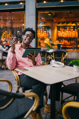 Laughing African freelancer joyfully lifting stylus during remote work session on tablet, representing tech satisfaction, motivation and creativity in mobile freelance job.