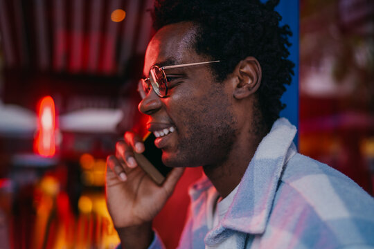 Profile of young man in red light talking on phone, immersed in mobile communication, highlighting personal tech usage in modern digital spaces with strong urban visual energy.