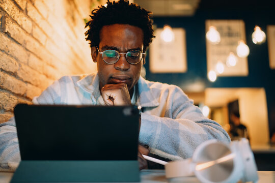 Concentrated man analyzing tablet screen in cafe, representing focused work session with digital tools, mobile connectivity, and thoughtful interaction with information on modern devices. - Powered by Adobe