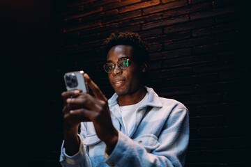 Young man smiling while interacting with smartphone, showcasing joy and satisfaction through digital communication in a minimalist, moody space. © BullRun