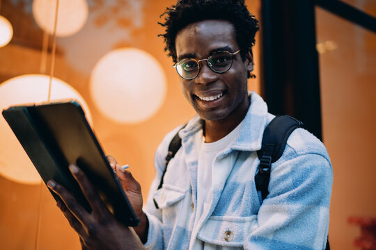 Casual man smiling at camera while holding tablet and stylus, showcasing human-centered tech interaction, creative independence, and approachable design in modern tech use.