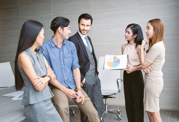 Business team discusses a project while one member presents a colorful chart. The group stands together, sharing ideas and feedback, creating a dynamic and collaborative professional environment.