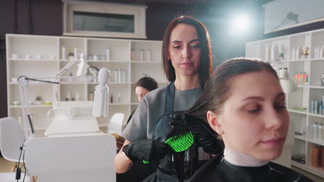 caucasian stylist brushing and detangling young client's hair with green brush in bright salon, gentle care and smoothing motion, shelves and lighting create professional family-friendly atmosphere,