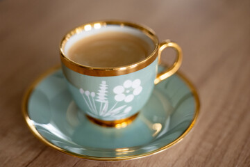 Elegant blue-and-gold porcelain cup filled with coffee on a matching saucer. Classic floral design creating a calm, relaxing and luxurious coffee moment.