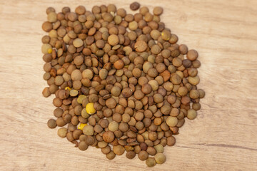 Pile of dry brown lentils on a wooden surface. Natural food ingredient photo ideal for packaging, product listings, recipes and healthy nutrition content.