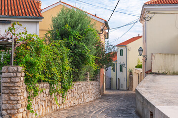 Charming mediterranean village street with stone path and lush greenery. Town of Krk, Krk island, Croatia