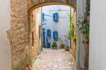 Charming narrow alleyway with rustic stone walls and blue shuttered windows. Town of Krk, Krk island, Croatia
