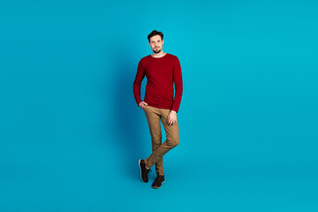 Young man in red sweater and khaki pants poses casually against a blue background in a stylish fashion portrait