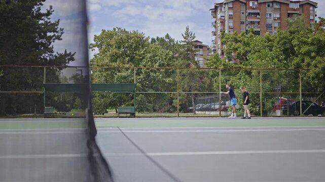A man and a woman, friends, engage in a friendly game of tennis on an outdoor court. They are enjoying a fun and active summer day, staying fit and socializing together.