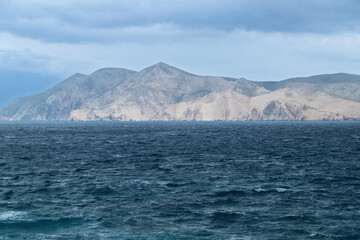 Stormy sea with overcast sky and mountainous landscape in the distance. View of Prvic island, Croatia
