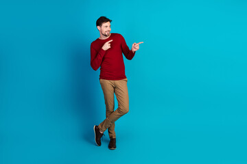 Young handsome man in red sweater poses against blue background pointing with a friendly smile for casual fashion lifestyle and advertising use