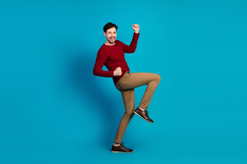 Obraz premium Young man in red sweater jumping with joy against blue background for lifestyle fashion advertising and promo