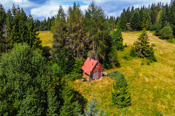 Aerial drone view of a small, isolated wooden hut next to the yellow trail to Turbacz peak in the Gorce Mountains, Poland. Remote nature and hiking concept.