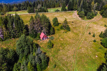 Aerial drone view of a small, isolated wooden hut next to the yellow trail to Turbacz peak in the Gorce Mountains, Poland. Remote nature and hiking concept.