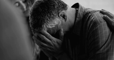 Man reacts emotionally during therapy session, eyes closed and mouth tense as another participant...