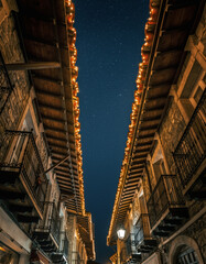 Obraz premium calle estrecha de un casco antiguo, iluminada con luces navideñas cálidas que bordean los tejados y balcones de edificios de piedra y madera, creando un ambiente festivo y acogedor durante la noche.