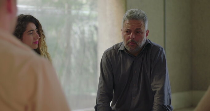 Man receives emotional support from group therapy members, seated in circle as participants place hands on his back and arms, offering comfort during vulnerable moment - Powered by Adobe