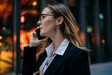 Young woman in formal suit speaking on smartphone outdoors, close side view showing concentration and control in professional phone conversation