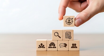 Hand placing a wooden block with target icon on top of a pyramid of blocks representing business goals and objectives