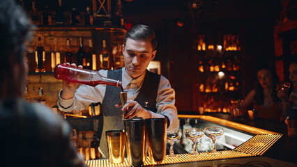 Skilled bartender pouring alcohol in special cup making cocktail in night bar.