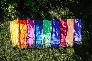 AI Generated - Row of colorful scarves sitting on top of a lush green field, with plants in the background. Professional stock photography. Stock photo. High-resolution. High-res. Premium quality.