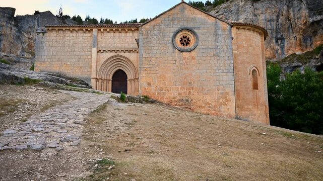The hermitage of Saint Bartolome rises against canyon cliffs in the canyon of Rio Lobos in Soria. its stone walls and Gothic arch revealed in a smooth panoramic shot of this historic Templar sanctuary
