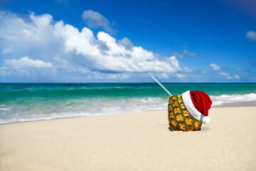 Santa Claus Hat on pina colada cocktail with pipe on tropical sandy beach. Christmas celebration
