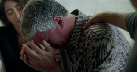 Man breaks down in therapy session, covering face with hands as group members offer comfort with hand on shoulder in scene of deep emotional release and support