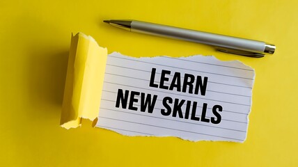 A silver pen rests on a torn piece of lined paper with the words learn new skills written in bold black letters against a vibrant yellow background