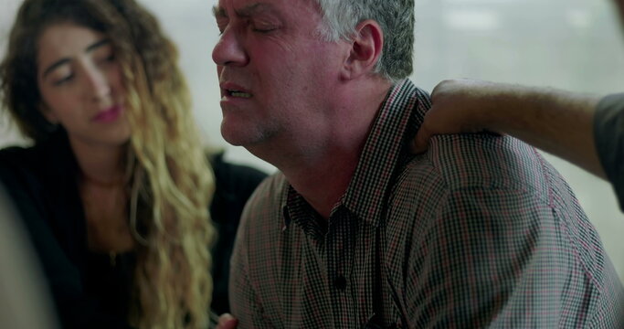 Man breaks down in therapy session, covering face with hands as group members offer comfort with hand on shoulder in scene of deep emotional release and support - Powered by Adobe