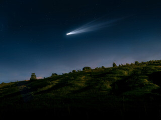 Comet in the sky visible to the naked eye. Bright tail of a comet over a hill. Astronomical observation of a space object.