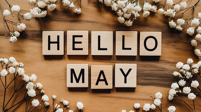 Wooden letter blocks spelling out hello may arranged on a rustic wooden surface surrounded by delicate white baby s breath flowers creating a charming spring greeting