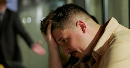 Man clutching head in distress after confrontation in modern office, experiencing emotional...