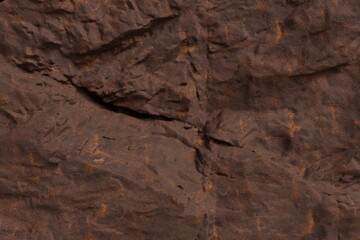 Textured brown rock face, showcasing a rugged and uneven surface with numerous cracks and shadowed crevices. Earthy tones, natural geological detail