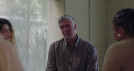 Man speaks emotionally during group therapy session, surrounded by peers in quiet circle as he...