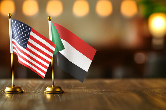 United States USA and Sudan small desk flags on wooden table - diplomatic relations concept with copy space