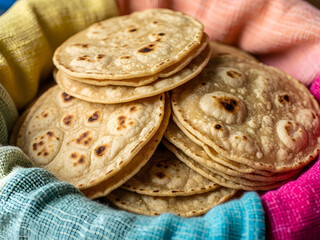 Stack of freshly made corn tortillas resting in a colorful woven basket