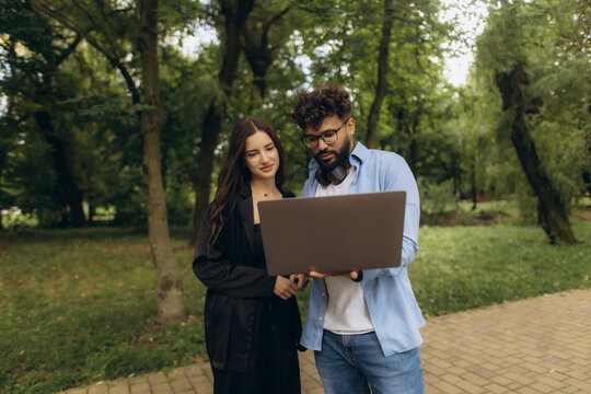Multiracial couple collaborating on laptop in park - Powered by Adobe