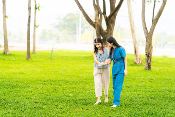 Asian nurse and elderly female patient standing in park and holding hands. Concept of care for elderly in retirement. Health service center.