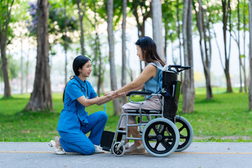 Asian female nurse assists and cares for elderly female patient sitting in wheelchair receiving physical therapy in nursing home park. Health concept.