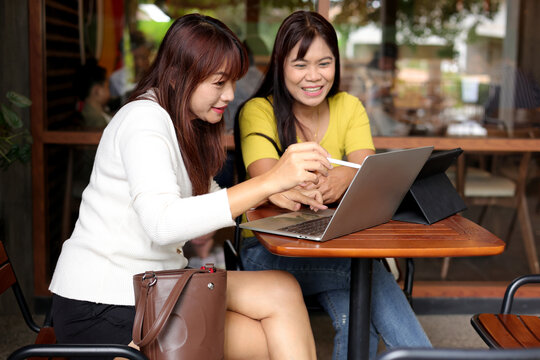 Two Asian Women Collaborating with Laptop and Tablet in Modern Cafe
