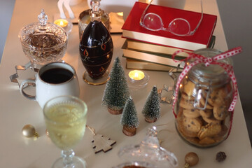 Cookie jar, tea, wine, nuts, books, lit candles and Christmas decorations on the table. Cozy Christmas hygge at home. Selective focus.