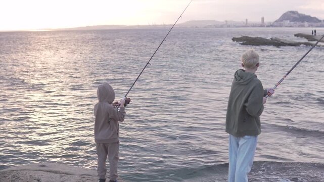 Children fishing with fishing rods by the sea at sunset. Spain